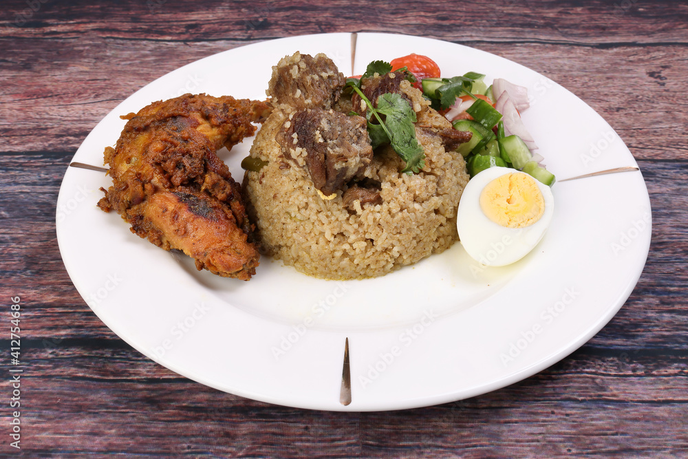 Beef Biryani Tehari with boiled egg coriander leaf garnish chicken curry pot roasted leg tomato cucumber onion chili coriander salad on white plate set over rustic wood background Beef Biryani Tehari with boiled egg coriander leaf garnish chicken curry pot roasted leg tomato cucumber onion chili coriander salad on white plate set over rustic wood background