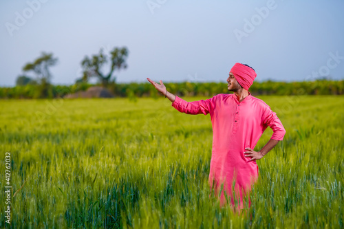 Young indian farmer standing at green wheat field