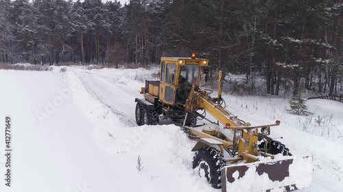 Aerial view of Snowblower Grader Clears Snow Covered Road in field next to the forest. Cemetery in the forest. Hard winter weather conditions. 
