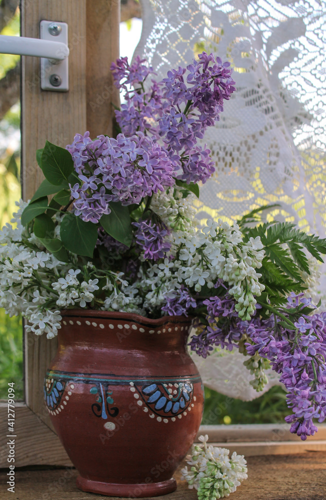 lilac in a clay pot on the window with a view of nature