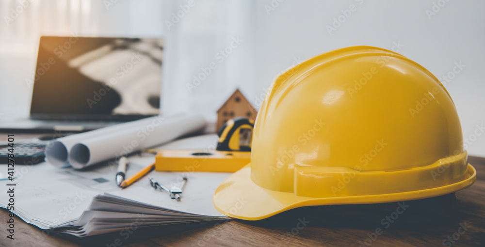 yellow hard hat safety helmet placed on a work desk with a design plan of the house Including engineering equipment. yellow hard hat safety helmet placed on a work desk with a design plan of the house Including engineering equipment.
