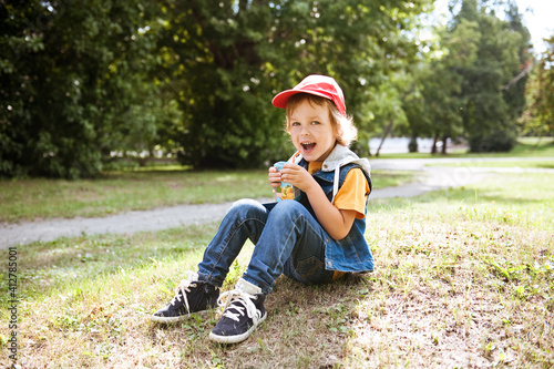 Happy child drinking juice out of a box on the street.