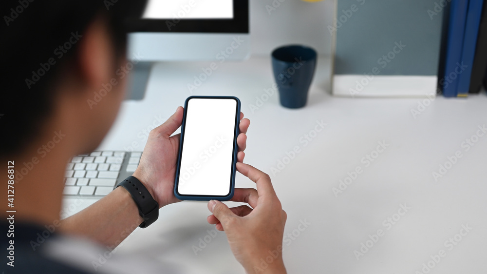 Close up view of young man holding smart phone with empty screen on his office desk.