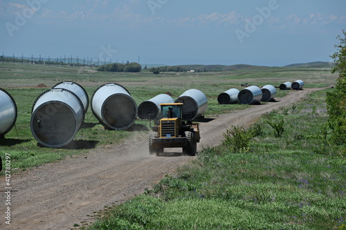 Zhambyl region, Kazakhstan - 05.15.2013 : The tractor rides along the road in a field where parts of wind turbines are laid out