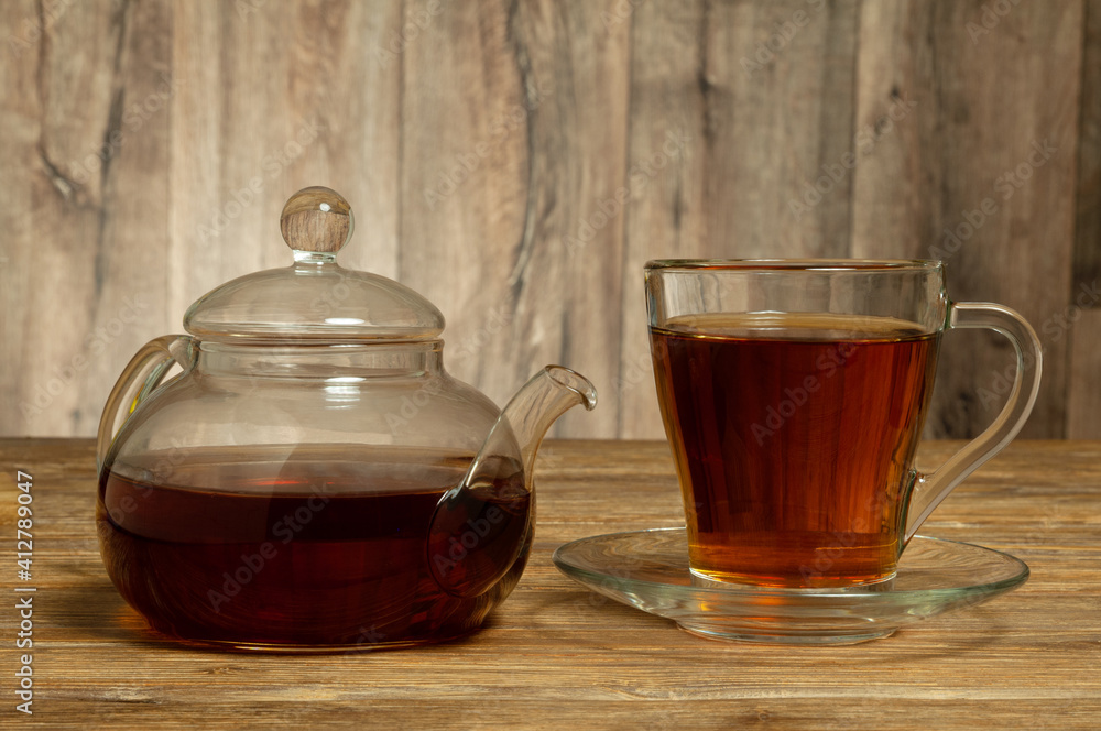 Glass teapot and glass cup with saucer with tea on wooden table. Close-up Glass teapot and glass cup with saucer with tea on wooden table. Close-up