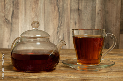 Glass teapot and glass cup with saucer with tea on wooden table. Close-up