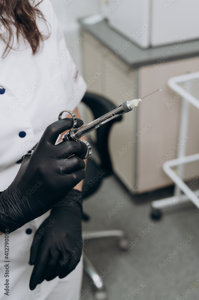 a dentist wearing black gloves holds a metal syringe in his hand