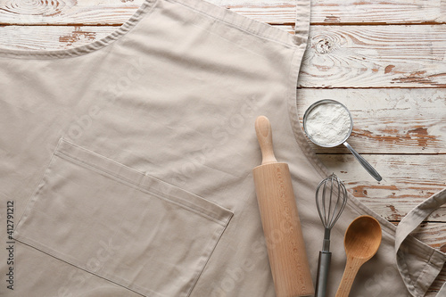 Fototapeta Apron, utensils and flour on wooden background, closeup