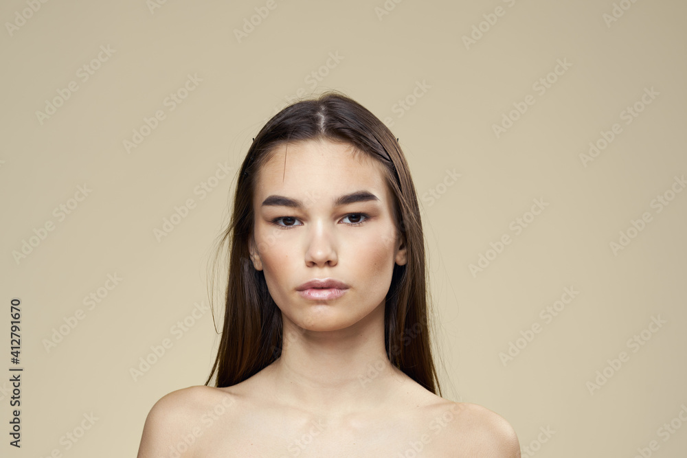 Woman with bared shoulders dark hair clean skin makeup beige background Woman with bared shoulders dark hair clean skin makeup beige background