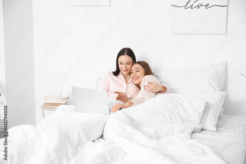 Fototapeta premium Young lesbian couple with laptop in bed at home