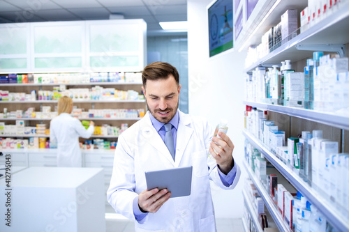 Professional handsome male pharmacist working in pharmacy store or drugstore. Checking medicines on his tablet computer. Healthcare and apothecary.