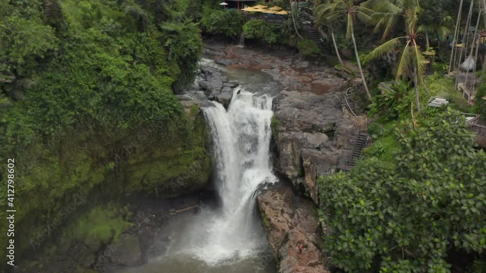 Aerial shot flying towards a large waterfall in the Bali jungle with outdoors restaurant on the cliff above Aerial shot flying towards a large waterfall in the Bali jungle with outdoors restaurant on the cliff above