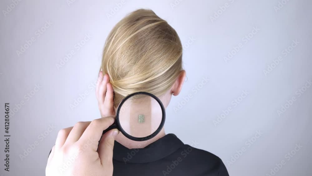 The woman shows his neck with a chip implanted which is studied with a magnifying glass. The concept of chipping and implantation of electronic technologies. Cybernetics and the nanofuture. Cyberpunk The woman shows his neck with a chip implanted which is studied with a magnifying glass. The concept of chipping and implantation of electronic technologies. Cybernetics and the nanofuture. Cyberpunk