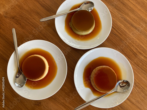 three white plates of delicious homemade sweet vanilla and green tea caramel custard dessert with silver spoons put on a brown wooden table
