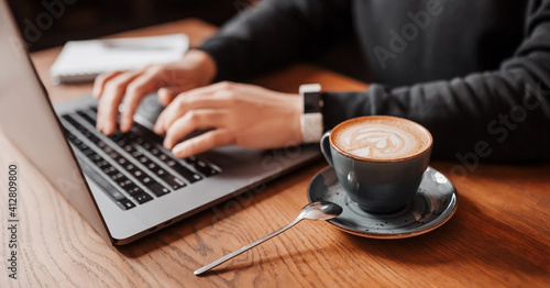 Handsome man working on laptop in the workplace. Businessman prints information at desk with coffee