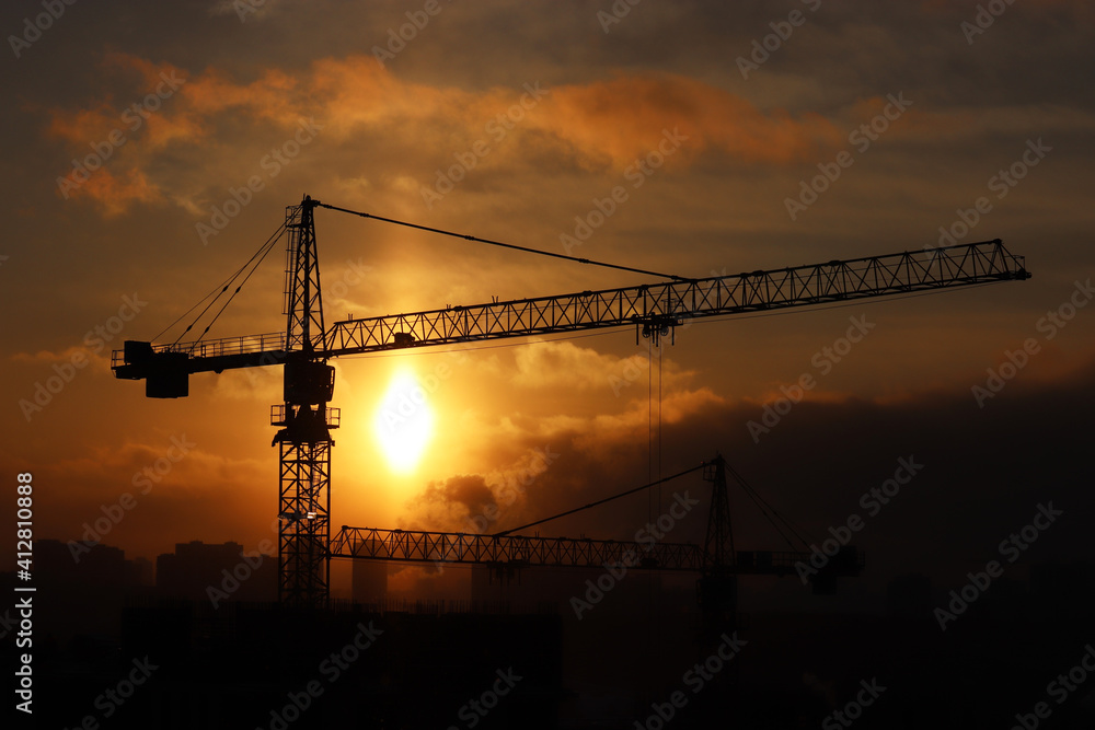 Silhouettes of construction cranes and unfinished residential buildings on sunset background. Housing construction, apartment block in city