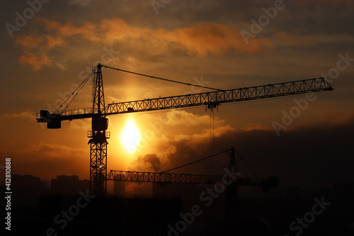 Silhouettes of construction cranes and unfinished residential buildings on sunset background. Housing construction, apartment block in city