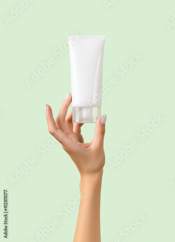 Womans hand holding white tube on pastel green background