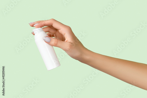 Womans hand holding white bottle on pastel green background