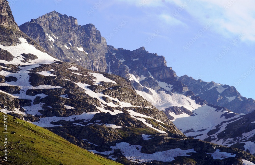 A close up, detailed shot of a mountain covered up with snows near a path filled with green grass under the blue sky.