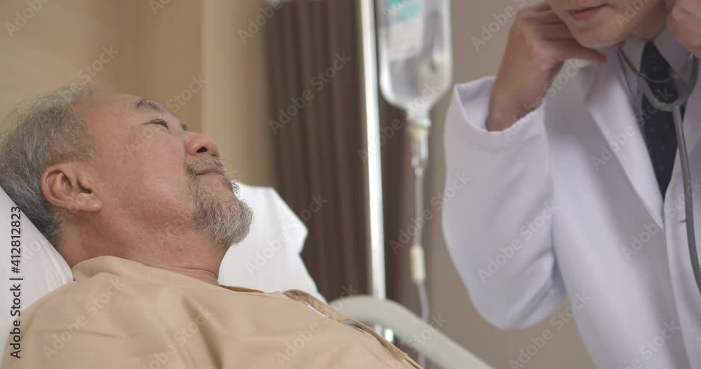 Asian older man patient sleeping in bed then a male doctor come to using stethoscope listen to the heartbeat to check up and female nurse adjusts IV flow in hospital. Senior people healthcare concept. Asian older man patient sleeping in bed then a male doctor come to using stethoscope listen to the heartbeat to check up and female nurse adjusts IV flow in hospital. Senior people healthcare concept.
