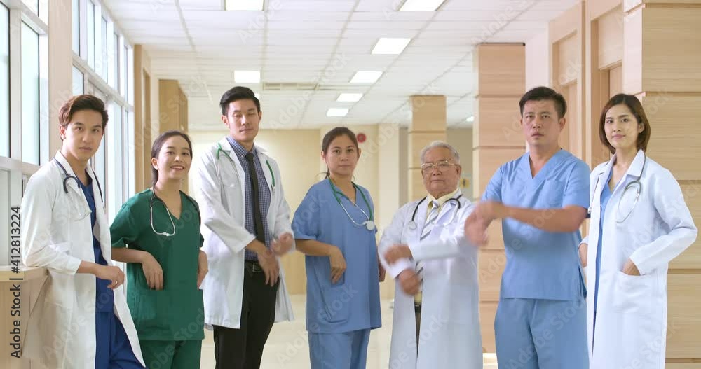 Tilt Down shot group of a Asian male and female doctors standing and cross their arms with a smile looking at camera in hospital hallway. Confident medical team ready to treating their patients. Tilt Down shot group of a Asian male and female doctors standing and cross their arms with a smile looking at camera in hospital hallway. Confident medical team ready to treating their patients.