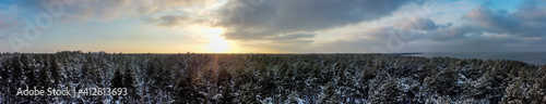 Sunset over snow-covered forest and sea at sunset in winter. Panoramic landscape.