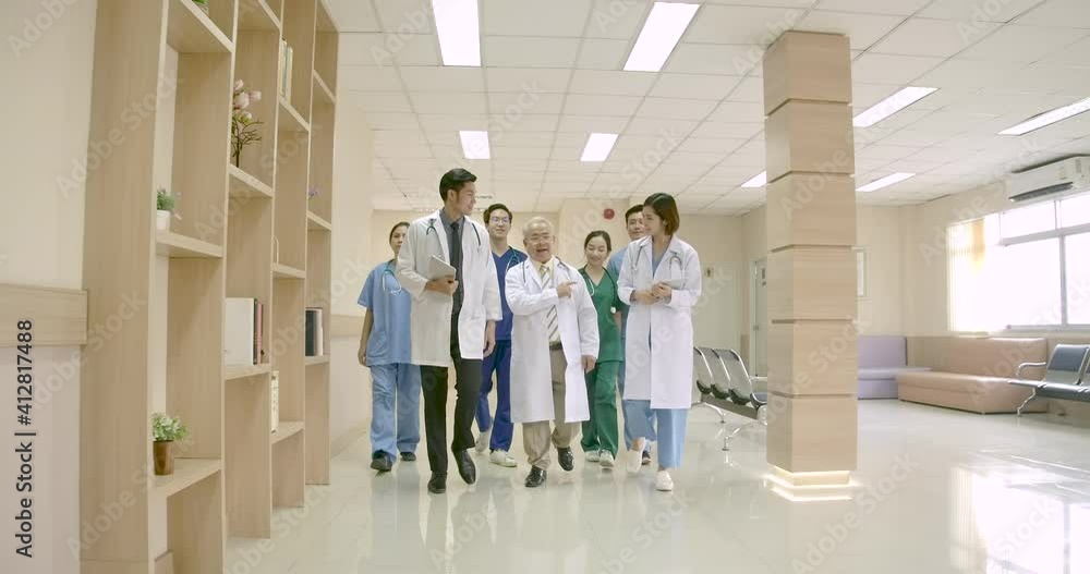 Dolly shot of A group of Asian male and female medical practitioners and senior doctor walking talking and giving opinions about treating patients in hospital hallway. medical and healthcare concept. Dolly shot of A group of Asian male and female medical practitioners and senior doctor walking talking and giving opinions about treating patients in hospital hallway. medical and healthcare concept.