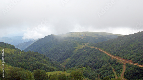 A magnificent view of foothills of mountains and snowy peak under the cloudy sky.