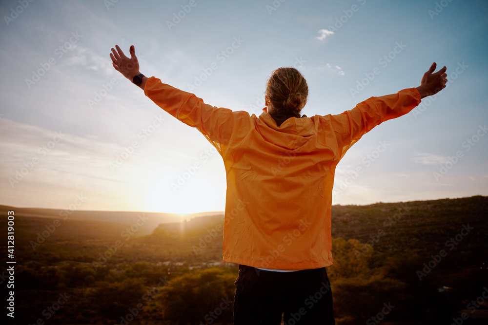 Rear view of young man standing on mountain with outstretched arms feeling relaxed after morning running in nature Rear view of young man standing on mountain with outstretched arms feeling relaxed after morning running in nature