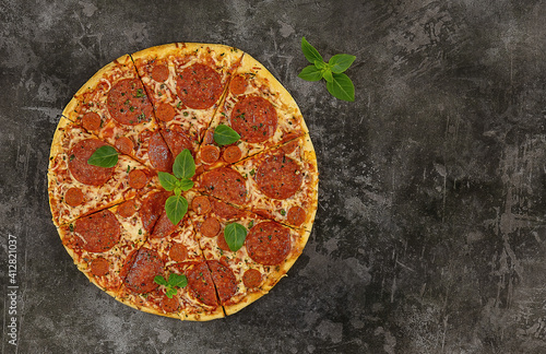 Tasty pepperoni pizza and fresh basil on dark background.