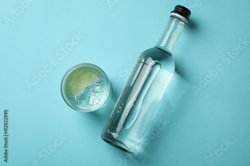 Bottle and glass of vodka with lime on blue background