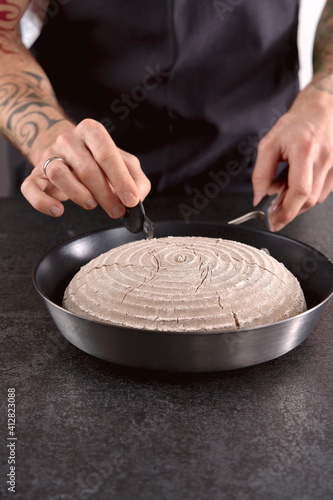 tattooed hands scoring proofed rye sourdough bread in cooking pan