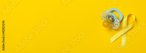 Pacifier and child cancer awareness ribbon on yellow background