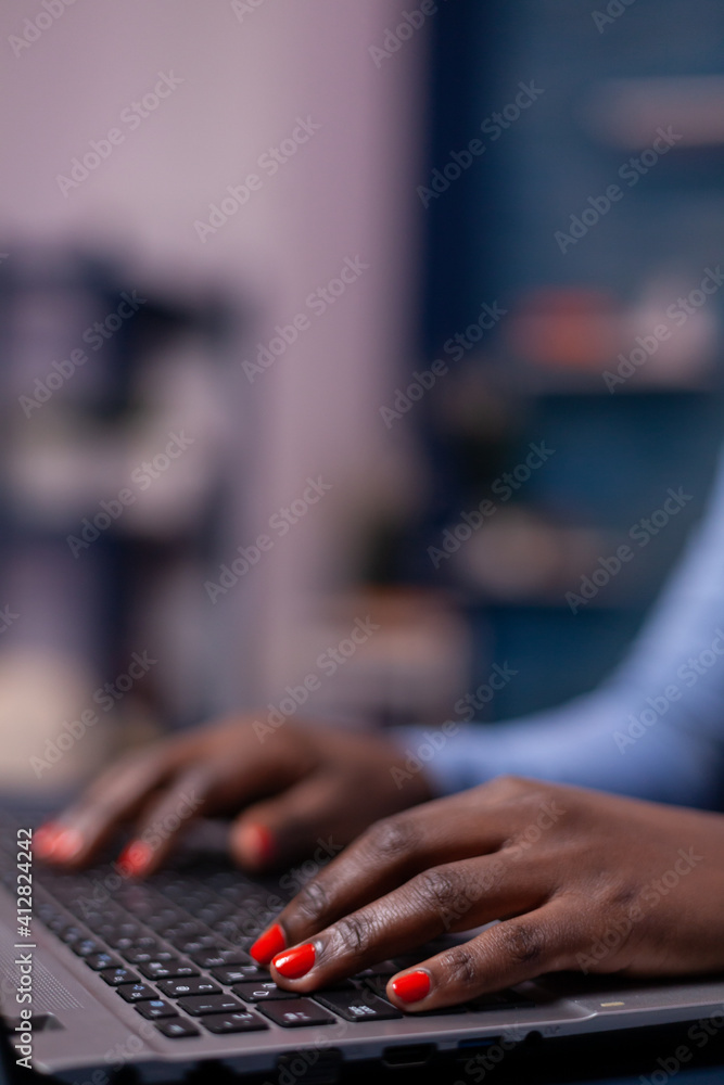 African american in living room using laptop computer sitting at desk at night. Employee using modern technology network wireless doing overtime. African american in living room using laptop computer sitting at desk at night. Employee using modern technology network wireless doing overtime.