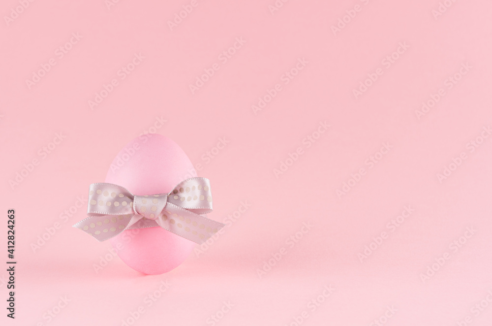 Gentle pink easter egg standing with grey bow on pastel pink background, copy space.