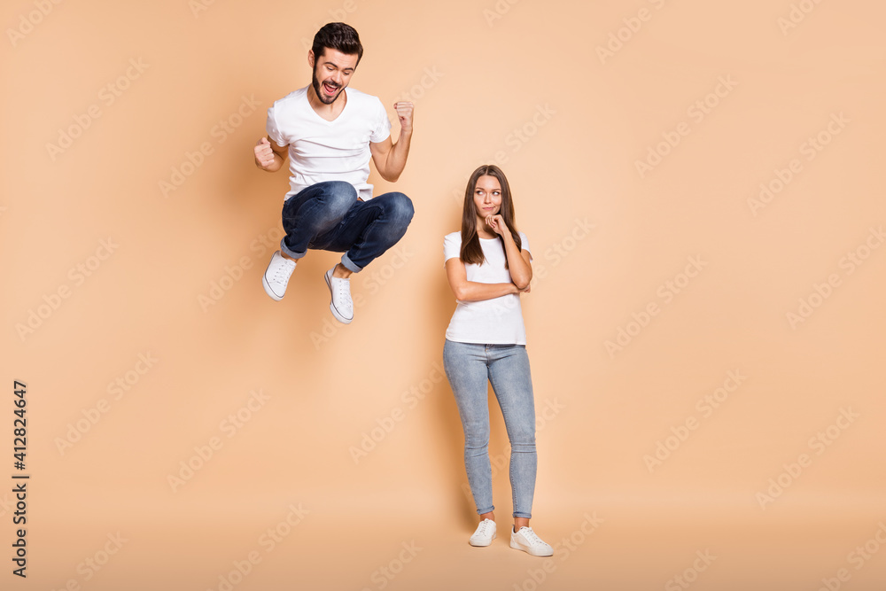 Full body photo of young couple he happy jump up rejoice victory she unhappy sad isolated over beige color background