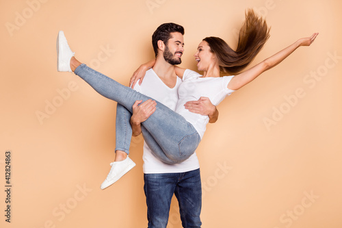Photo of pretty married couple dressed white t-shirts dancing he holding arms her looking each other isolated beige color background