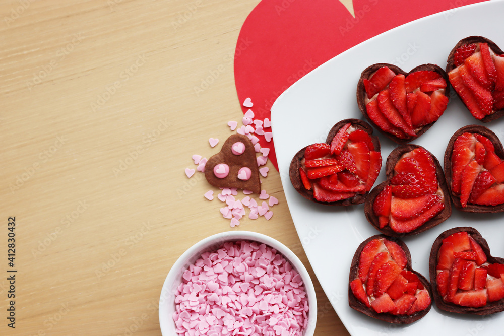 Valentine’s day dessert with copy space. Mini heart shaped chocolate tarts with fresh strawberries on a plate on a wooden table Valentine’s day dessert with copy space. Mini heart shaped chocolate tarts with fresh strawberries on a plate on a wooden table