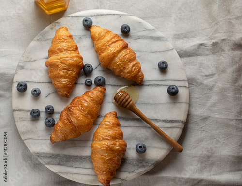 Homemade croissants with blueberries and honey on marble tray top view with copy space. High quality photo