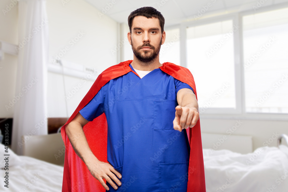 healthcare, profession and medicine concept - doctor or male nurse in blue uniform and red superhero cape pointing to camera over hospital ward background healthcare, profession and medicine concept - doctor or male nurse in blue uniform and red superhero cape pointing to camera over hospital ward background