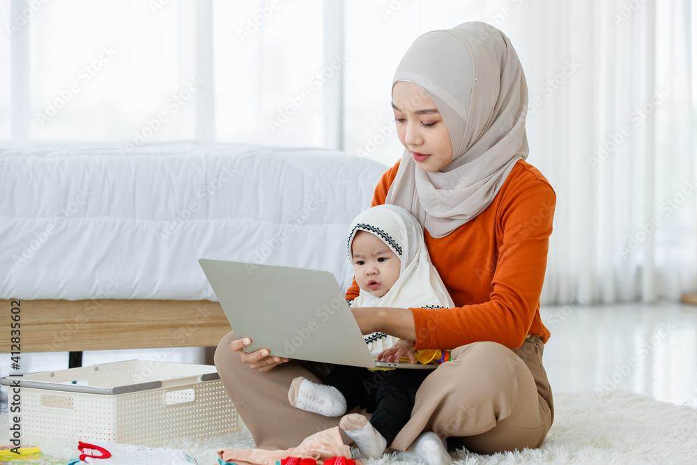 A cute and beautiful Asian Muslim mother work as an online seller working on laptop notebook computer and take care of her baby daughter in the same time A cute and beautiful Asian Muslim mother work as an online seller working on laptop notebook computer and take care of her baby daughter in the same time