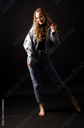 young woman poses with jeans barefoot. Full height, dark background