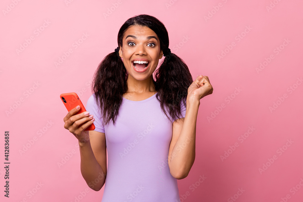 Photo of beautiful afro american brown tails hared woman raise fist hold phone win isolated on pink color background Photo of beautiful afro american brown tails hared woman raise fist hold phone win isolated on pink color background