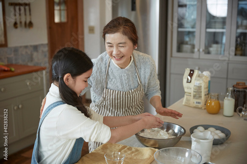 Happy adorable little child girl in apron enjoying cooking homemade pastry together with grandmother at home.