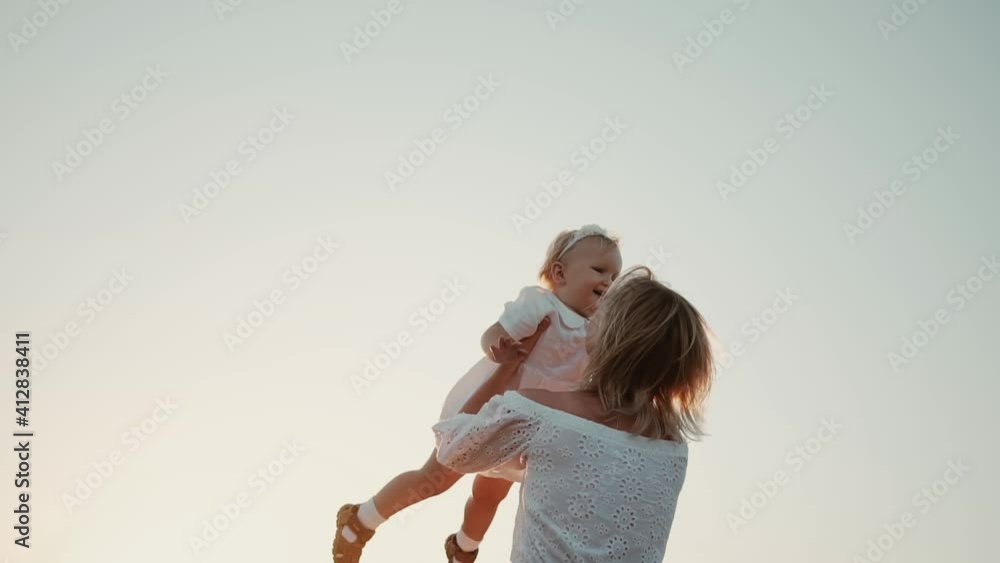 Happy beautiful family healthy. Child runs into hug mom lifting cute little daughter up and twists around himself in field at sunset, funny kid girl flying in mothers arms laughing having fun together Happy beautiful family healthy. Child runs into hug mom lifting cute little daughter up and twists around himself in field at sunset, funny kid girl flying in mothers arms laughing having fun together