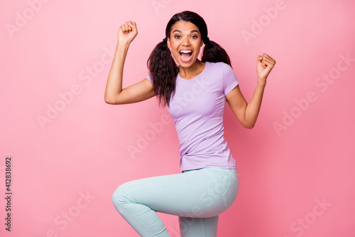 Profle side photo of astonished victorious afro american lady raise fists leg wear pants isolated on pink color background photo