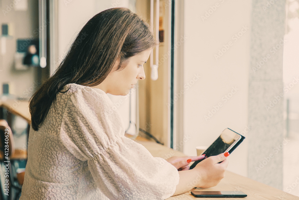 Focused young Caucasian woman using tablet while sitting at desk in co-working space. Medium shot. Communication concept Focused young Caucasian woman using tablet while sitting at desk in co-working space. Medium shot. Communication concept