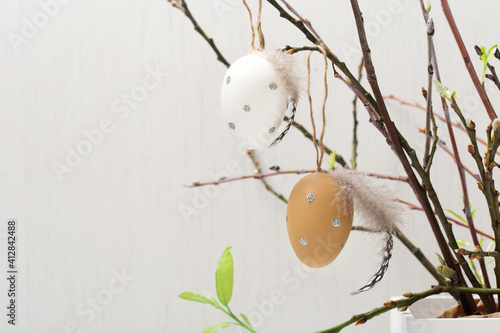 Easter holiday concept with cute handmade white eggs, tree branches, quail feathers and spring flowers on white wooden background.