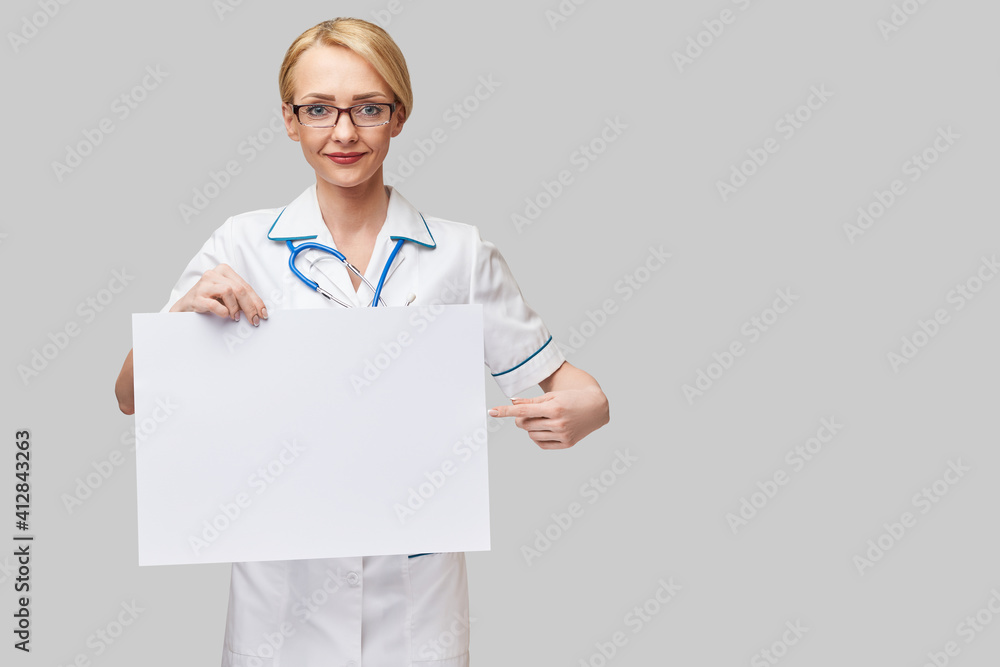 Female doctor holding a blank banner sign standing over grey background Female doctor holding a blank banner sign standing over grey background